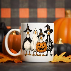 Pu&ograve; includere: Tazza in ceramica bianca con un design a tema Halloween. Raffigura quattro oche dei cartoni animati in costume: una strega, un fantasma, una zucca e uno scheletro. Le oche sono in piedi insieme. Lo sfondo include zucche e foglie autunnali.