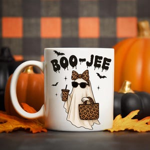 Pu&ograve; includere: Tazza in ceramica bianca con la scritta "BOO-JEE" in nero gocciolante. La tazza presenta un fantasma dei cartoni animati con occhiali da sole, un fiocco leopardato e porta una borsa e un caff&egrave; con stampa leopardata. Anche pipistrelli e stelle nere sono sulla tazza.