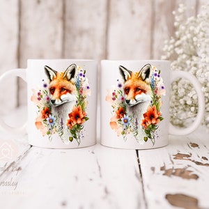 May include: Two white ceramic mugs with a watercolor design of a fox surrounded by flowers. The fox is orange and white with a black nose and eyes. The flowers are in shades of pink, purple, blue, and orange.