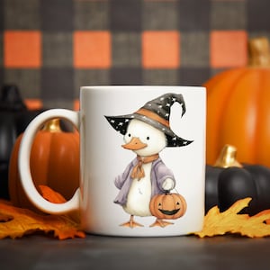 May include: White ceramic mug featuring a cartoon duck dressed as a witch for Halloween. The duck wears a black hat with white stars, a purple coat, and holds a jack-o'-lantern. Pumpkins and fall leaves are in the background.