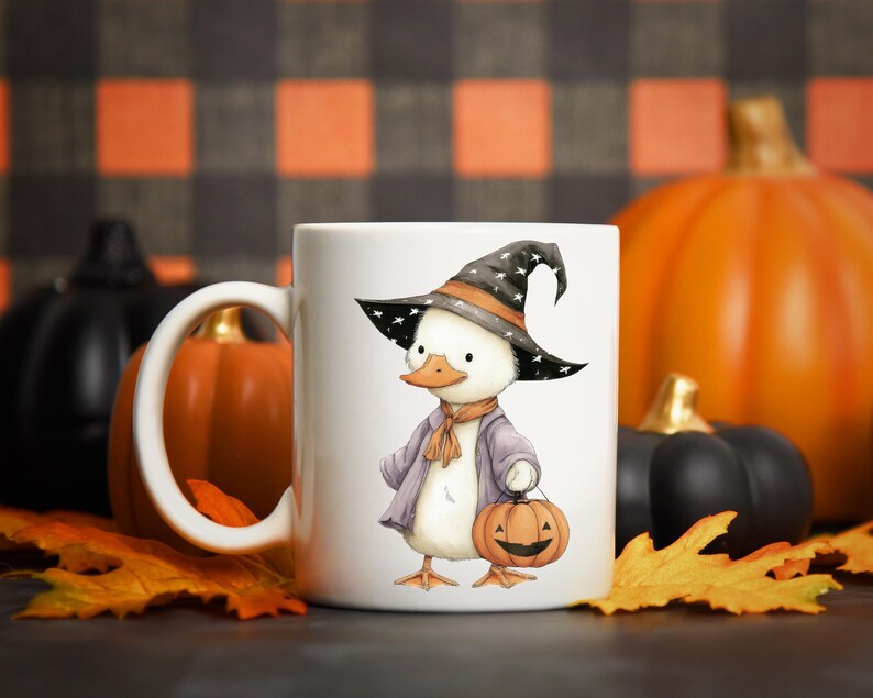 May include: White ceramic mug featuring a cartoon duck dressed as a witch for Halloween. The duck wears a black hat with white stars, a purple coat, and holds a jack-o'-lantern. Pumpkins and fall leaves are in the background.