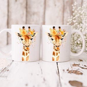 May include: Two white ceramic mugs with a watercolor design of a giraffe wearing a floral crown. The giraffe has brown spots and a light brown face. The flowers are yellow, orange, and blue.