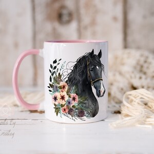 Pu&ograve; includere: Tazza in ceramica bianca con manico rosa. La tazza presenta un'illustrazione ad acquerello di una testa di cavallo nero con una ghirlanda di fiori intorno.
