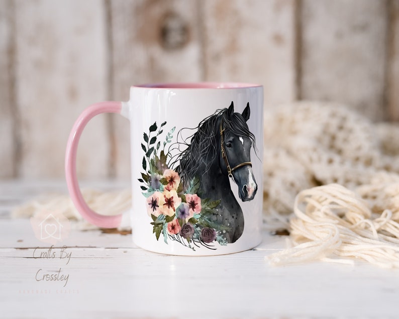 Pu&ograve; includere: Tazza in ceramica bianca con manico rosa. La tazza presenta un'illustrazione ad acquerello di una testa di cavallo nero con una ghirlanda di fiori intorno.