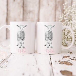 May include: Two white ceramic mugs with a black and white illustration of a lamb on each. The text "_Nikki_" is written in pink on the bottom of each mug.