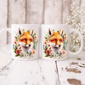 May include: Two white ceramic mugs with a fox illustration surrounded by watercolor flowers. The fox has orange fur, a white chest, and black eyes. The flowers are pink, white, and blue.