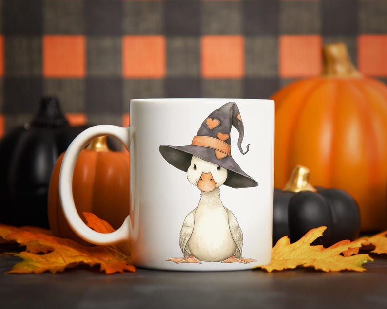May include: White ceramic mug featuring a watercolor illustration of a duck wearing a witch hat with orange heart accents. The background includes pumpkins and fall leaves, perfect for Halloween.