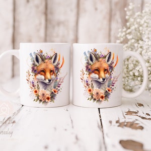 May include: Two white ceramic mugs with a fox wearing a floral crown design. The fox is surrounded by flowers and leaves in shades of orange, pink, purple, and green.