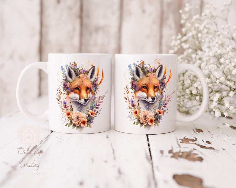 May include: Two white ceramic mugs with a fox wearing a floral crown design. The fox is surrounded by flowers and leaves in shades of orange, pink, purple, and green.