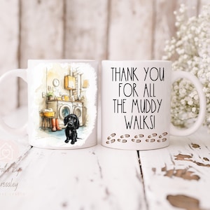 May include: Two white ceramic mugs. One mug features a watercolor illustration of a black dog in a laundry room. The other mug has the text "THANK YOU FOR ALL THE MUDDY WALKS!" with paw prints.