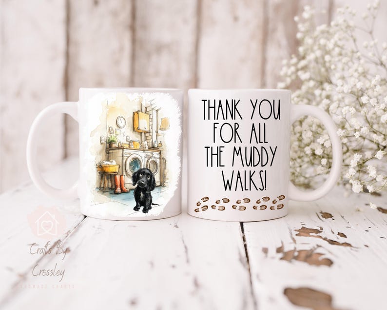 May include: Two white ceramic mugs. One mug features a watercolor illustration of a black dog in a laundry room. The other mug has the text "THANK YOU FOR ALL THE MUDDY WALKS!" with paw prints.