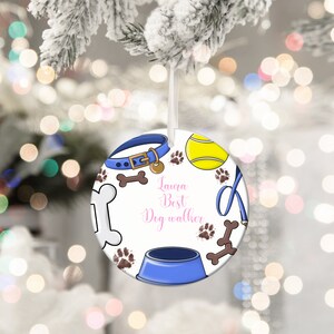 May include: Round white Christmas ornament with a blue dog collar, tennis ball, paw prints, and dog bone illustrations. The ornament has a blue dog bowl and the text "Laura Best Dog walker" in pink script.