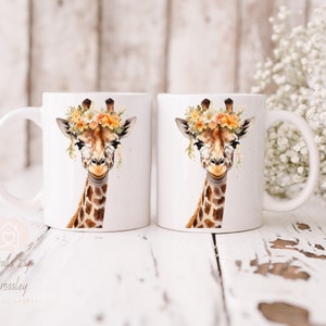 May include: Two white ceramic mugs with a giraffe wearing a flower crown printed on them. The giraffe has brown spots and a light brown face. The flowers are yellow, orange, and white.