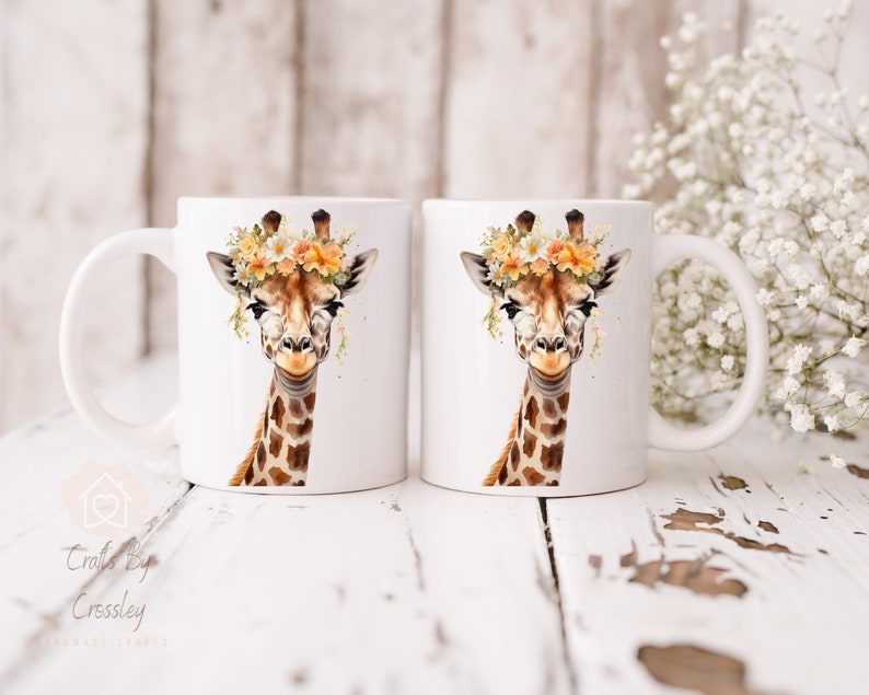 May include: Two white ceramic mugs with a giraffe wearing a flower crown printed on them. The giraffe has brown spots and a light brown face. The flowers are yellow, orange, and white.