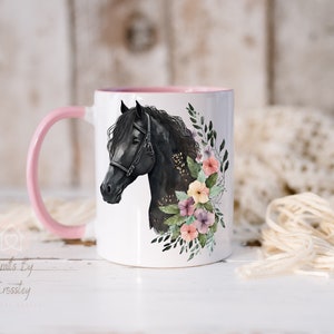 Pu&ograve; includere: Una tazza in ceramica bianca con un manico e un bordo rosa. La tazza presenta un cavallo nero con un design floreale in tonalit&agrave; di rosa, giallo e viola.