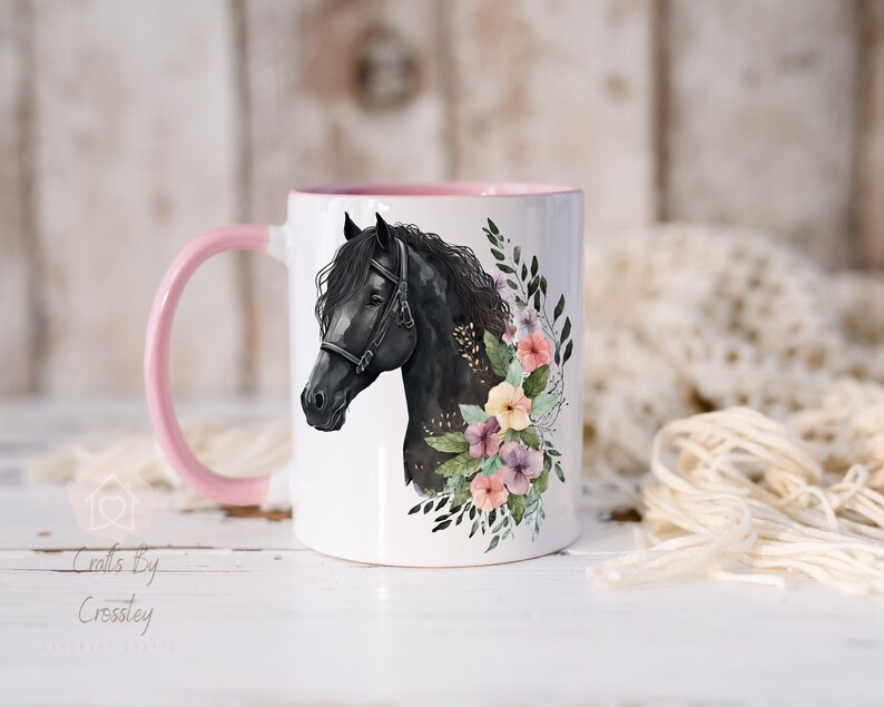 Pu&ograve; includere: Una tazza in ceramica bianca con un manico e un bordo rosa. La tazza presenta un cavallo nero con un design floreale in tonalit&agrave; di rosa, giallo e viola.