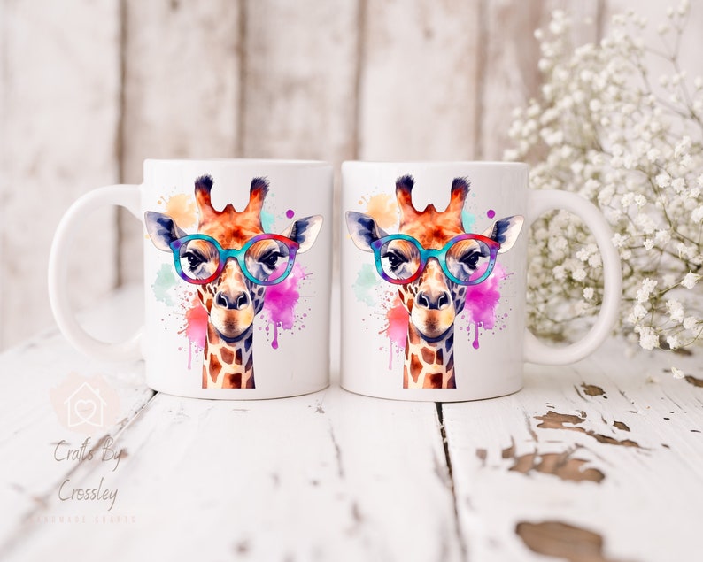 May include: Two white ceramic mugs with a watercolor design of a giraffe wearing glasses. The giraffe is surrounded by colorful paint splatters.