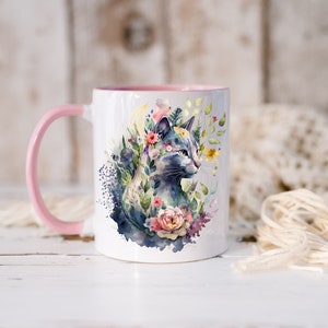 May include: White ceramic mug with a pink handle and a watercolor design of a cat surrounded by flowers. The cat is blue and gray with green eyes.
