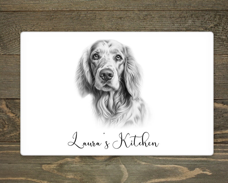 Pu&ograve; includere: Un tagliere rettangolare bianco con un ritratto dettagliato in bianco e nero di un cane. Il testo "Laura's Kitchen" &egrave; scritto in elegante corsivo sotto il ritratto del cane. Lo sfondo &egrave; una superficie di legno.