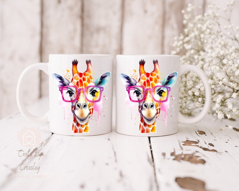 May include: Two white ceramic mugs with a watercolor illustration of a giraffe wearing pink glasses. The giraffe is painted in shades of orange, yellow, and pink.