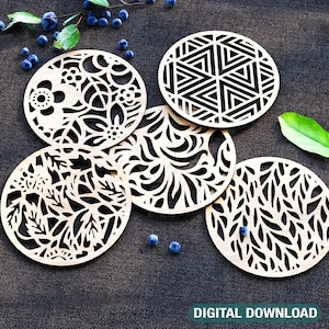 Puede incluir: Cinco posavasos de madera cortados con láser con diseños intrincados. Los posavasos presentan patrones geométricos y motivos florales. Los posavasos están dispuestos sobre una superficie gris oscura.