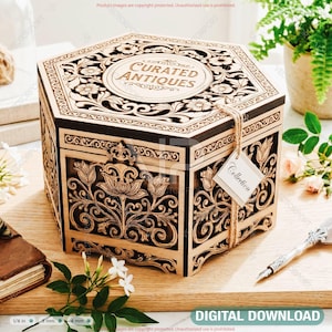 Puede incluir: Caja hexagonal de madera con intrincados grabados florales y el texto "CURATED ANTIQUES" en la tapa. Una etiqueta que dice "Collection" cuelga de la caja. La caja se exhibe sobre una superficie de madera con un diario encuadernado en cuero y una pluma decorativa.