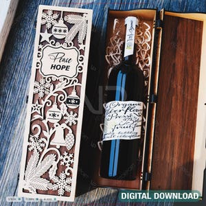 Könnte beinhalten: Eine Holzgeschenkbox mit einem lasergeschnittenen Design mit Schneeflocken, Ornamenten und den Worten "Peace HOPE". Im Inneren befindet sich eine Flasche Bio-Holunderblüten-Fruchtmarmelade auf Holzwolle. Die Box ist aus dunklem Holz.