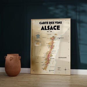 May include: A vintage-style map of the Alsace wine region in France. The map is printed on a beige background with brown and red lines indicating the different wine-producing areas. The title "Carte des Vins d'Alsace" is printed in black at the top of the map.