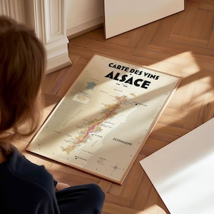 May include: A vintage-style map of the Alsace wine region in France. The map is printed on cream-colored paper and features a detailed illustration of the vineyards and towns. The title "Carte des Vins Alsace" is printed in bold black letters at the top of the map.