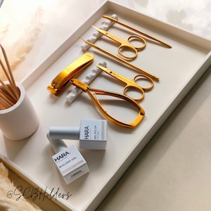Pode incluir: Uma bandeja branca com ferramentas de manicure douradas e dois frascos de esmalte de unha. Os frascos s&atilde;o etiquetados como "HARA Professional" e cont&ecirc;m "Builder Gel" e "Gel Polish" com uma camada superior.