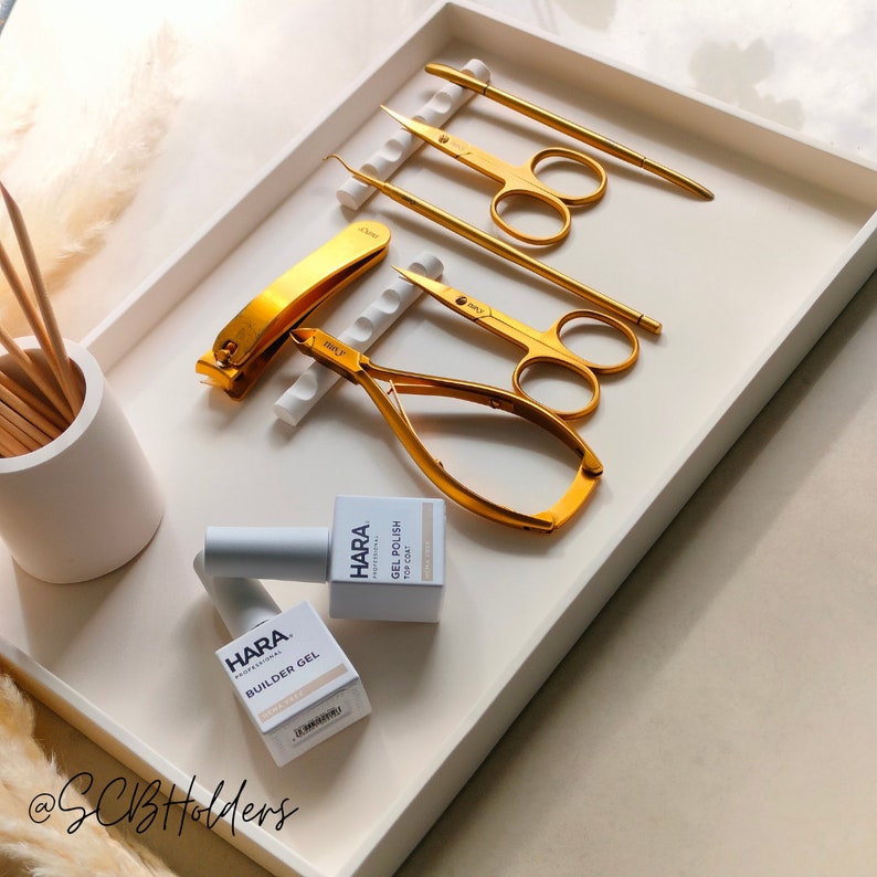 Pode incluir: Uma bandeja branca com ferramentas de manicure douradas e dois frascos de esmalte de unha. Os frascos s&atilde;o etiquetados como "HARA Professional" e cont&ecirc;m "Builder Gel" e "Gel Polish" com uma camada superior.