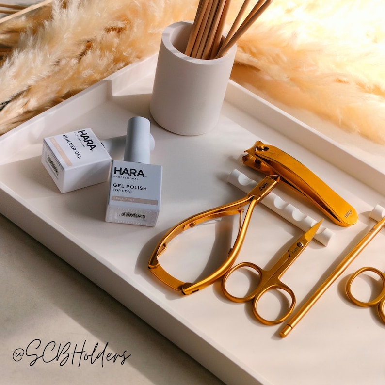 Pode incluir: Uma bandeja branca com ferramentas de manicure douradas, duas garrafas de esmalte de unha transparente com etiquetas brancas que dizem "HARA Professional", e um suporte de cer&acirc;mica branca com palitos de madeira. As etiquetas das garrafas dizem "Builder Gel" e "Gel Polish Top Coat".