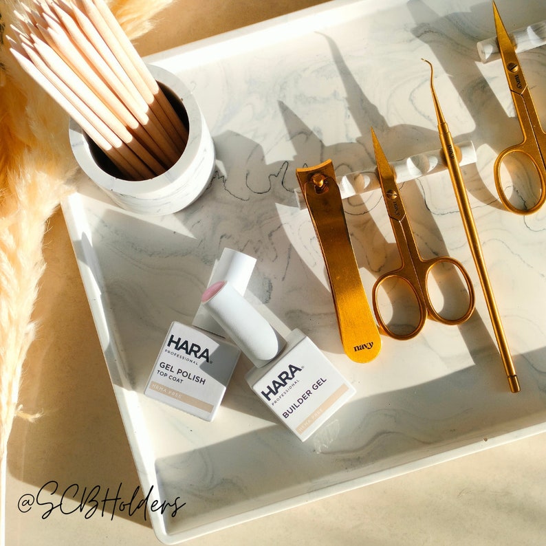 Pode incluir: Uma bandeja de m&aacute;rmore branco com duas garrafas de esmalte de unha, uma com a etiqueta "HARA Professional Gel Polish Top Coat" e a outra com a etiqueta "HARA Professional Builder Gel". A bandeja tamb&eacute;m cont&eacute;m um cortador de unhas dourado, um par de tesouras de cut&iacute;cula douradas e um empurrador de cut&iacute;cula dourado.