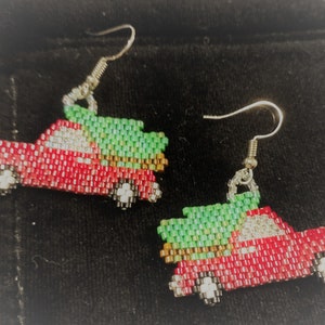 May include: A pair of red truck earrings with green trees on top. The trucks are made of beads and the earrings are silver.
