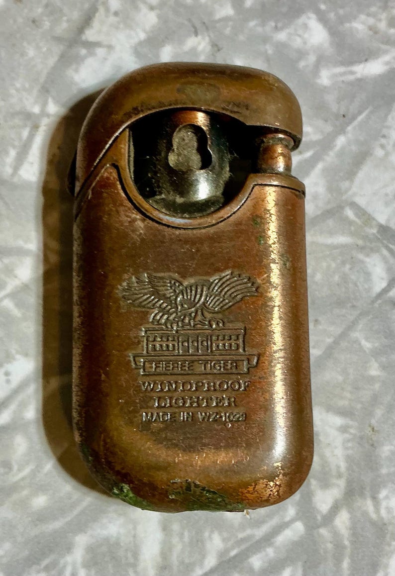 May include: Vintage bronze-colored "Fieree Tiger" windproof lighter. The lighter features an embossed eagle emblem above the text "Fieree Tiger" and "Windproof Lighter". The lighter is marked "Made in WZ-1029".
