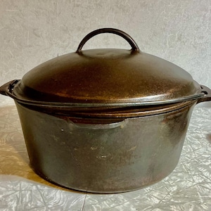 May include: A dark brown cast iron Dutch oven with a matching lid. The pot has a rounded shape with two handles on the sides and a loop handle on the lid. The pot is designed for cooking and baking.