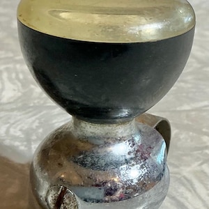 May include: A vintage, chrome-plated bell with a black and gold top. The bell has a rounded base and a curved handle. The top portion is black, with a gold-colored cap. A screw is visible on the side of the bell.