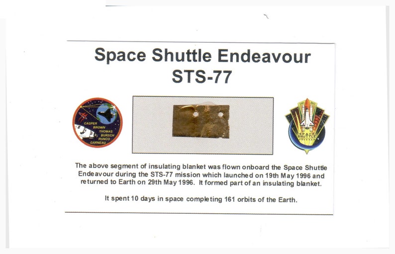 May include: A white card with the text 'Space Shuttle Endeavour STS-77' in black text. Below the text are three images: a round patch with a space shuttle and the names 'Casper, Brown, Thomas, Runco, Garneau', a piece of gold-colored material with two holes, and a patch with a space shuttle and the text 'Space Shuttle.' The text below the images reads: 'The above segment of insulating blanket was flown onboard the Space Shuttle Endeavour during the STS-77 mission which launched on 19th May 1996 and returned to Earth on 29th May 1996. It formed part of an insulating blanket. It spent 10 days in space completing 161 orbits of the Earth.'
