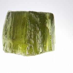 May include: A large, translucent green crystal with a rough, textured surface. The crystal has a natural, organic shape and is a beautiful example of a gemstone.