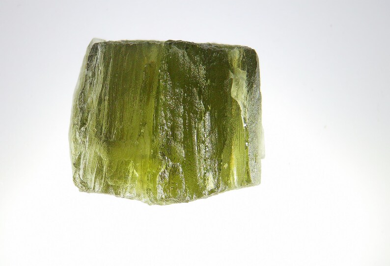 May include: A large, translucent green crystal with a rough, textured surface. The crystal has a natural, organic shape and is a beautiful example of a gemstone.