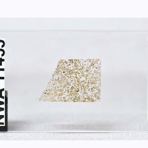 Puede incluir: Primer plano de una pequeña muestra de roca marrón claro etiquetada como "NWA 11455 Eucrita-unbr."