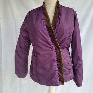 May include: A plum-coloured jacket with a brown velvet collar and trim. The jacket has a quilted appearance and is displayed on a mannequin. The trim is accented with a purple, scalloped edge.