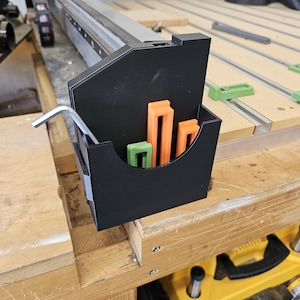 May include: A black plastic tool organizer with a variety of tools, including a wrench, a green and orange ruler, and a green and orange spacer. The organizer is mounted on a wooden surface.