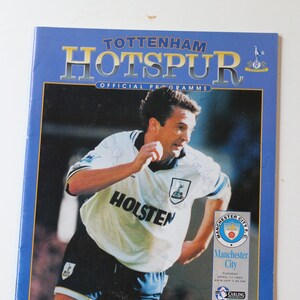 May include: A blue and white Tottenham Hotspur football program from April 11, 1995, featuring a photo of a soccer player in a white jersey with the Holsten logo. The program advertises a match against Manchester City, sponsored by PremiumSearch.
