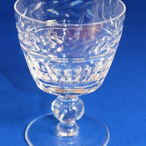 May include: A clear, cut-glass goblet with a round base, a bulbous stem, and a detailed bowl. The bowl features intricate patterns and designs. The glass is set against a blue background.