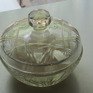 May include: A clear glass candy dish with a matching lid, featuring a faceted diamond-shaped knob handle. The exterior surface of both the bowl and the lid is decorated with a pressed geometric starburst pattern and cross-hatched grid detailing.