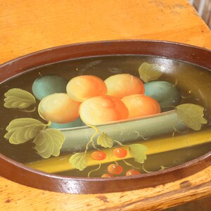 May include: An oval wooden tray with a painted design of fruit in a bowl. The fruit is painted in shades of orange, yellow, and green. The tray has a brown wooden rim and two handles.