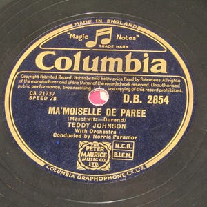 Puede incluir: Disco de vinilo Columbia vintage con la canción "Ma'Moiselle De Paree" de Teddy Johnson. El disco tiene una etiqueta azul marino y dorada con el logotipo de Columbia y texto, incluyendo "Made in England". El disco es de 78 RPM.