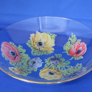 May include: A clear glass bowl with a gold rim features a floral design of pink, yellow, and white anemones on a green leafy background.