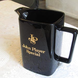 May include: Black ceramic pitcher with a gold logo that reads "John Player Special" and a gold "JP" monogram.